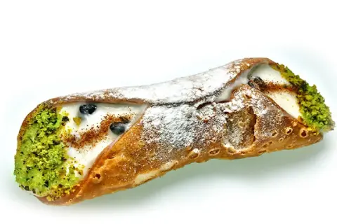 Sycylijskie dania: chrupiąca rurka cannoli z kremem, pistacjami i borówkami, posypana cukrem pudrem.