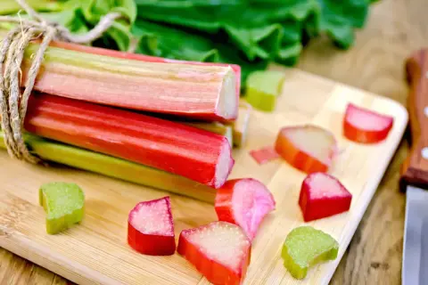 Pamiętaj, kiedy rabarbar jest trujący – liście są niebezpieczne! Na desce leżą pocięte łodygi, gotowe do spożycia.