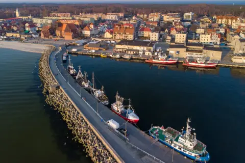 Port w Helu poza sezonem. Spokojne wody, zacumowane kutry i statki, a w tle miasto i las.