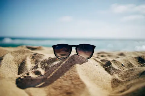 Okulary przeciwsłoneczne na piaszczystej plaży, w tle morze i błękitne niebo. Idealne na wakacje, gdy obowiązuje opłata klimatyczna nad morzem.