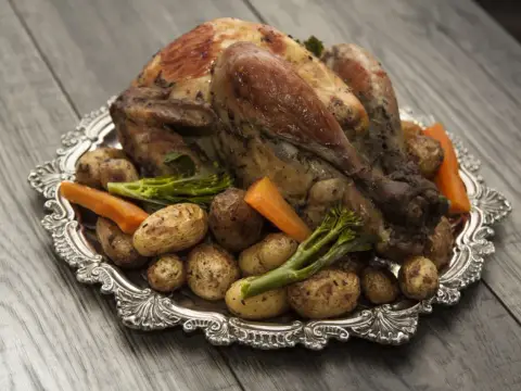 Pieczona perliczka z ziemniakami, marchewką i brokułami na ozdobnej tacy.