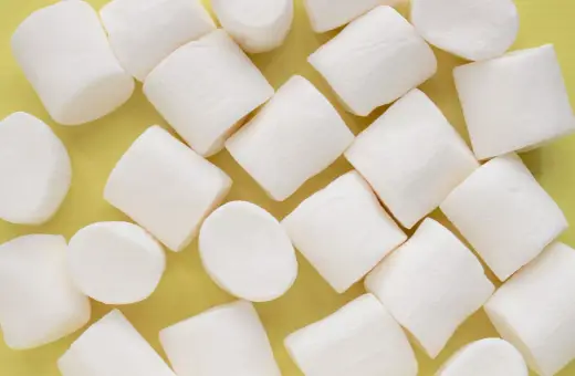 Białe, puszyste pianki marshmallow ułożone na żółtym tle. Pańska skórka, co to za słodka przyjemność!
