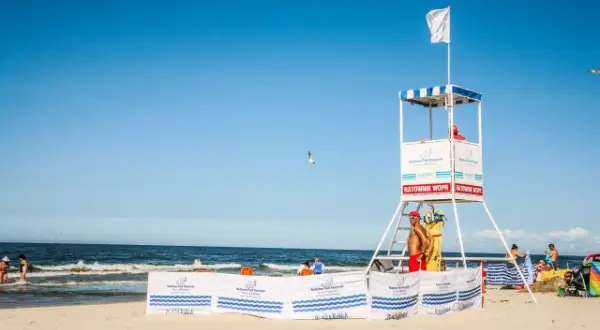 Biała flaga nad morzem oznacza bezpieczną kąpiel. Ratownik czuwa z wieży ratowniczej na plaży.