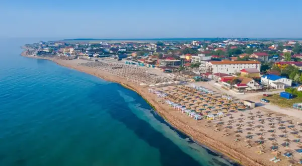 Widok na plażę z rzędami leżaków i parasoli. W tle zabudowania kurortowe. Woda w morzu czarnym jest ciepła, idealna do kąpieli.