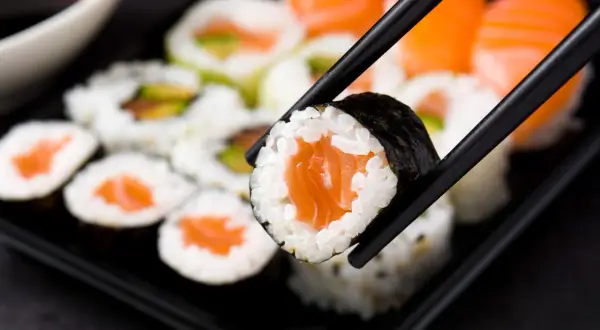 Chopsticks trzymają kawałek sushi z łososiem. Czy sushi jest zdrowe? Tak, jeśli wybierasz świeże składniki i umiarkowane porcje ryżu.