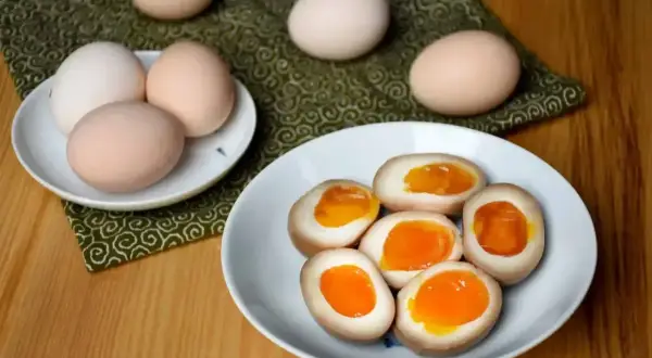 Na talerzu jajka do ramenu z płynnym, pomarańczowym żółtkiem. Obok surowe jajka.