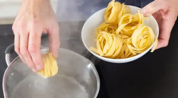 Ręka wkłada porcję tagliatelle do wrzącej wody. Czy makaron gotujemy pod przykryciem? Zobacz, jak zacząć gotowanie.