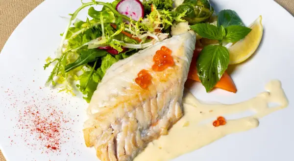 Filet morszczuka z ikrą, podany z sałatką, warzywami i sosem. Czy morszczuk jest zdrowy? Tak, to chuda ryba bogata w białko.