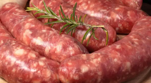 Świeża, surowa kiełbasa włoska z gałązką rozmarynu i czosnkiem w tle.