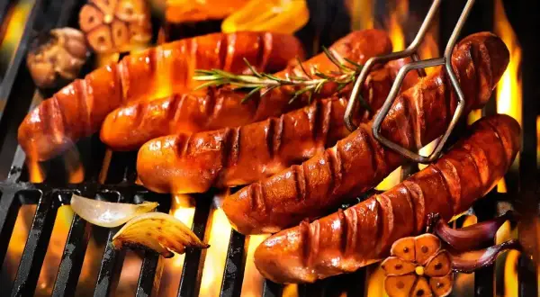Soczysta kiełbasa na grilla, skwiercząca na ogniu, z dodatkiem czosnku i rozmarynu. Idealna na letnie wieczory.