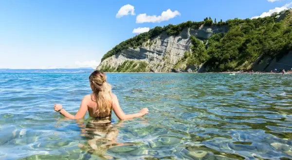Kobieta w wodzie, podziwiająca klify. To dowód, że Słowenia ma dostęp do morza, oferując piękne plaże i krystalicznie czystą wodę.