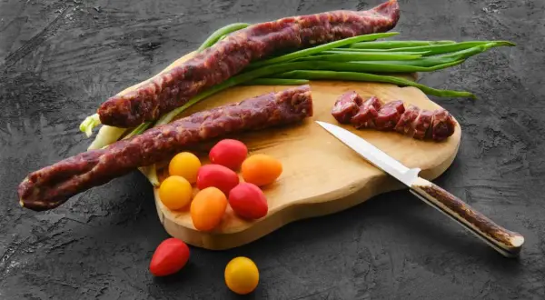 Dwa długie kabanosy, pokrojone plastry, pomidorki i szczypiorek na desce. Czy kabanosy są zdrowe? To pytanie zadaje sobie wielu.