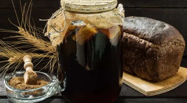 Słoik z ciemnym napojem, obok bochenek chleba i kłosy. Czy kwas chlebowy zawiera alkohol?