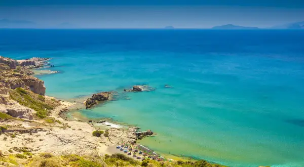 Malownicza zatoka na wyspie Kos, z turkusową wodą, skalistymi klifami i plażą z leżakami.