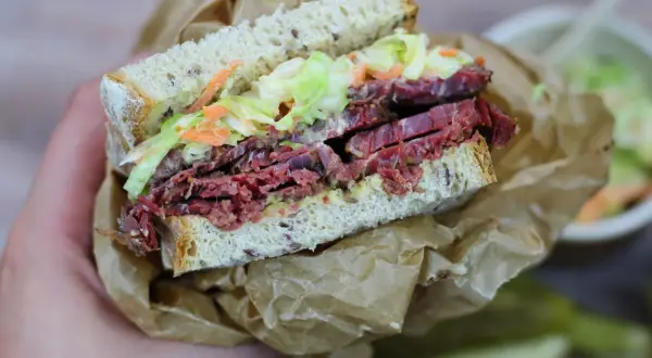 Pyszna kanapka z pastrami, z chrupiącą surówką i ziarnistym pieczywem, zawinięta w papier.