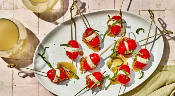 Kolorowe szaszłyki z pomidorkami koktajlowymi i mozzarellą, polane sosem. Idealne zdrowe przekąski na przyjęcie.