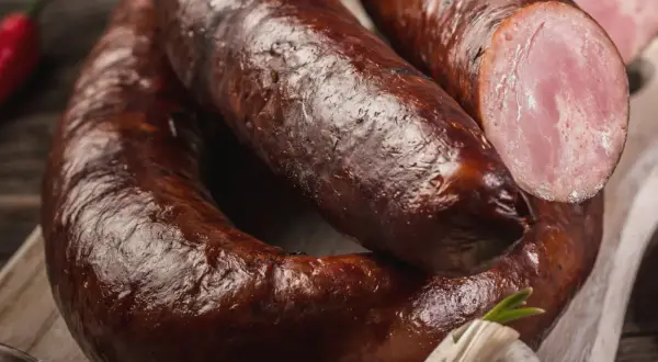 Aromaticzna kiełbasa lisiecka, wędzona i rumiana, z widocznym przekrojem ukazującym soczyste mięso. Obok czosnek i papryczka chili.