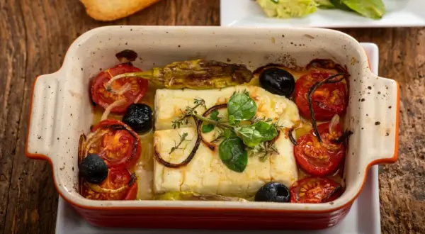Pyszna pieczona feta z pomidorkami, oliwkami i ziołami w ceramicznym naczyniu. Idealna na lekki posiłek.