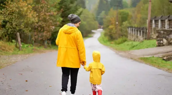 Mama i dziecko w żółtych płaszczach idą za rękę mokrą drogą. Nawet w deszczowe dni Jastarnia oferuje atrakcje, jak spacery po malowniczych okolicach.