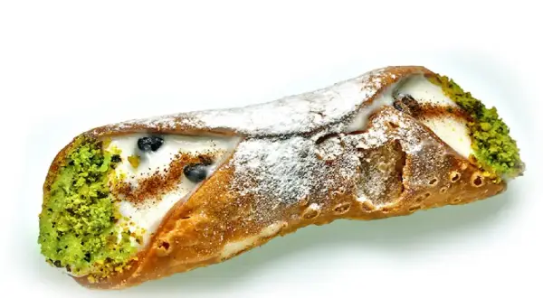 Sycylijskie dania: chrupiąca rurka cannoli z kremem, pistacjami i borówkami, posypana cukrem pudrem.