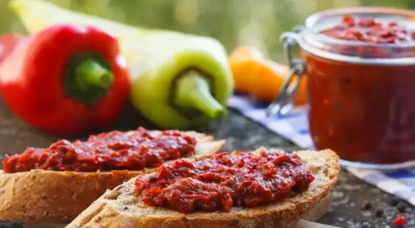 Chleb z pyszną pastą z pieczonej papryki, obok słoiczek i świeże papryki.