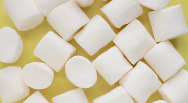 Białe, puszyste pianki marshmallow ułożone na żółtym tle. Pańska skórka, co to za słodka przyjemność!
