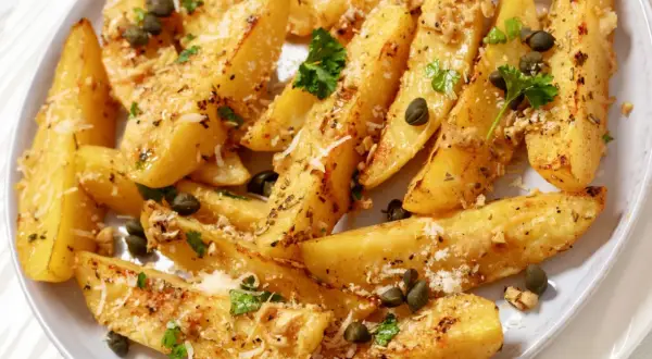 Ziemniaki po grecku, pieczone ćwiartki ziemniaków z ziołami, kaparami i parmezanem, wyglądają apetycznie.