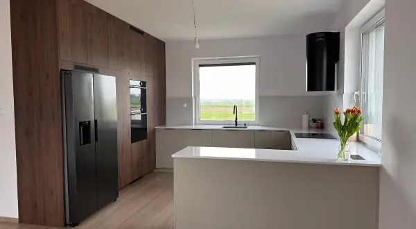 Nowoczesna kuchnia z zabudową w drewnie, wyspą i czarnym okapem. Idealne miejsce na przygotowanie dań haute cuisine.