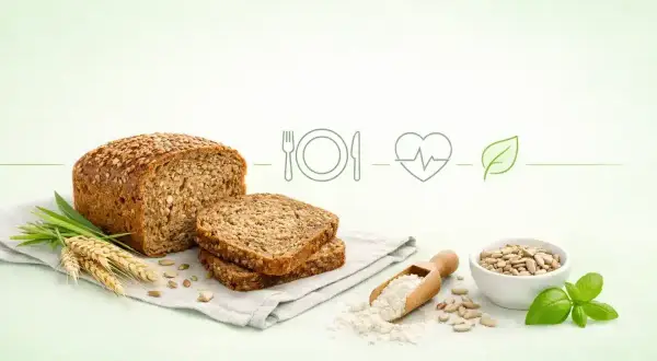 Bochenek pełnoziarnistego chleba z nasionami, obok kromki, kłosy zboża, mąka, słonecznik i bazylia. To symbol najzdrowszy chleb.