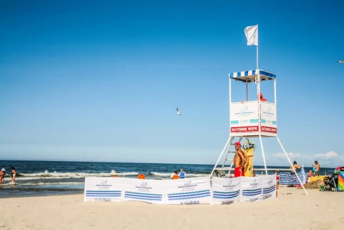Biała flaga nad morzem oznacza bezpieczną kąpiel. Ratownik czuwa z wieży ratowniczej na plaży.