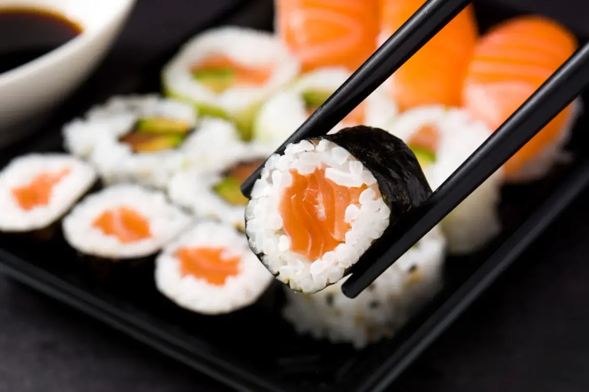 Chopsticks trzymają kawałek sushi z łososiem. Czy sushi jest zdrowe? Tak, jeśli wybierasz świeże składniki i umiarkowane porcje ryżu.