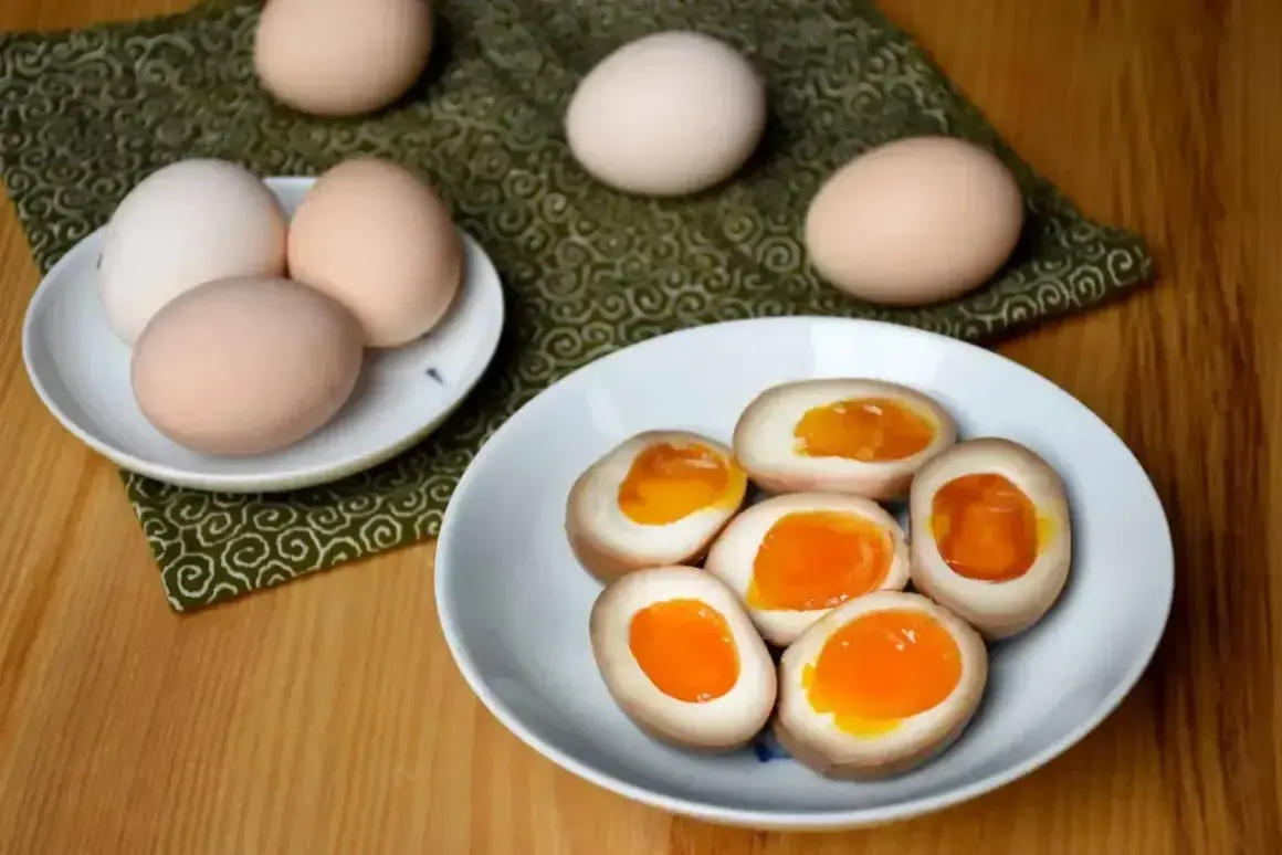 Na talerzu jajka do ramenu z płynnym, pomarańczowym żółtkiem. Obok surowe jajka.