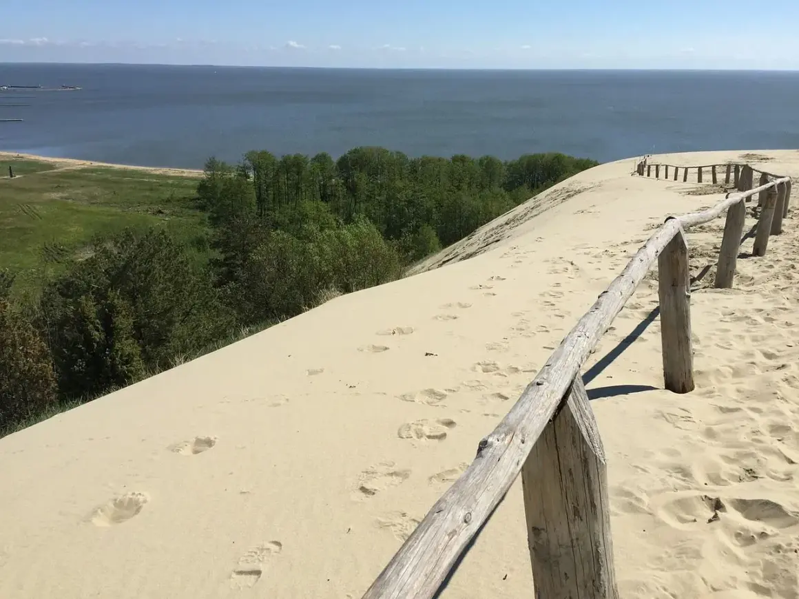 Piaskowe wydmy nad Bałtykiem, gdzie ślady stóp prowadzą do morza. Ciekawe, ile km ma morze bałtyckie, by dotrzeć do horyzontu?