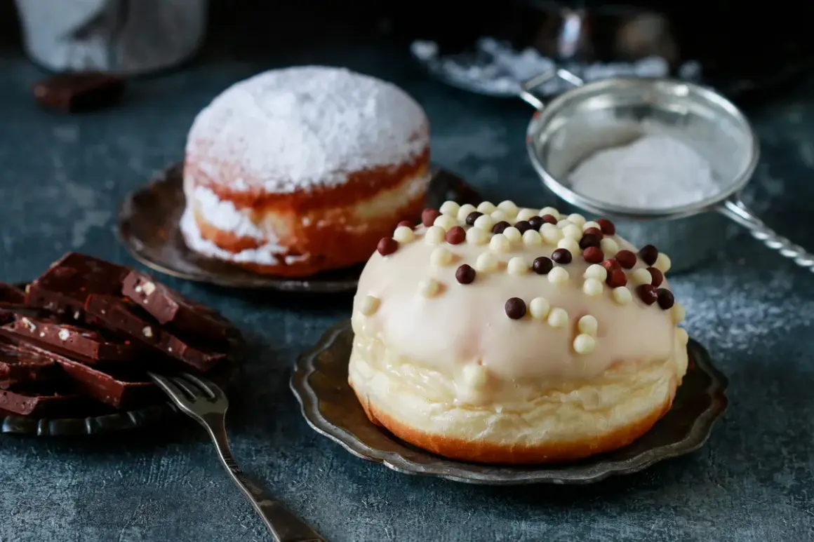 Dwa pączki: jeden oprószony cukrem pudrem, drugi polany lukrem i posypany kuleczkami. Pyszna pokusa, choć pączek kcal może przyprawić o zawrót głowy.