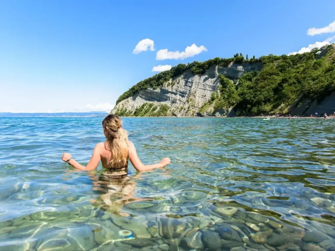 Kobieta w wodzie, podziwiająca klify. To dowód, że Słowenia ma dostęp do morza, oferując piękne plaże i krystalicznie czystą wodę.