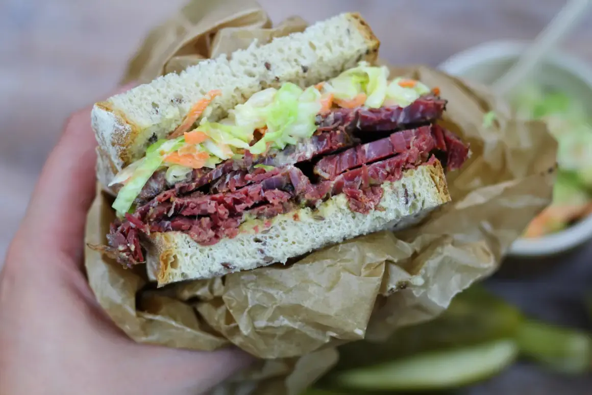 Pyszna kanapka z pastrami, z chrupiącą surówką i ziarnistym pieczywem, zawinięta w papier.