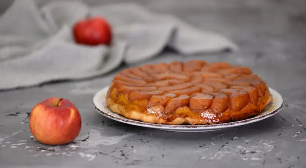 Apetyczna tarta tatin przepis na pyszny deser z karmelizowanymi jabłkami. Obok leży świeże jabłko.