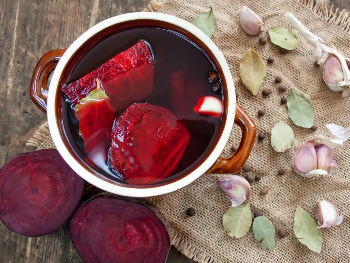 Zakwas z buraków przepis siostry Anastazji w garnku, obok buraki, czosnek, liście laurowe i ziele angielskie.