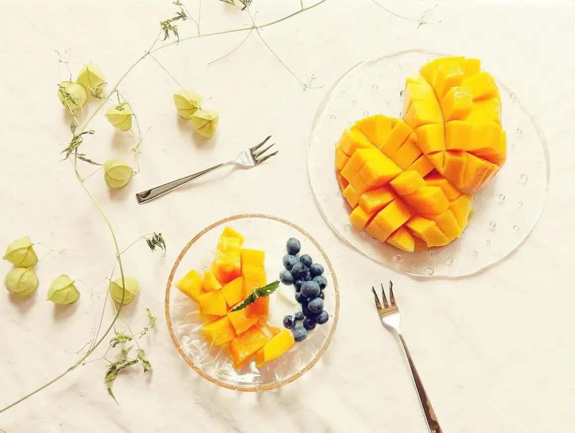 Słodkie mango pokrojone w kostkę, idealne do jedzenia z jagodami i jogurtem. Obok gałązka z zielonymi pąkami.