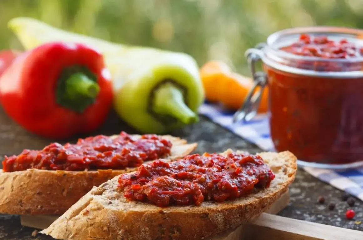 Chleb z pyszną pastą z pieczonej papryki, obok słoiczek i świeże papryki.