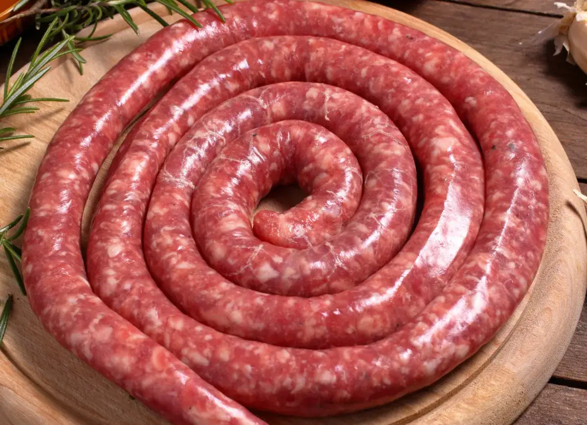 Surowa, zwinięta w spiralę kielbasa włoska, ozdobiona gałązkami rozmarynu, czeka na przygotowanie.