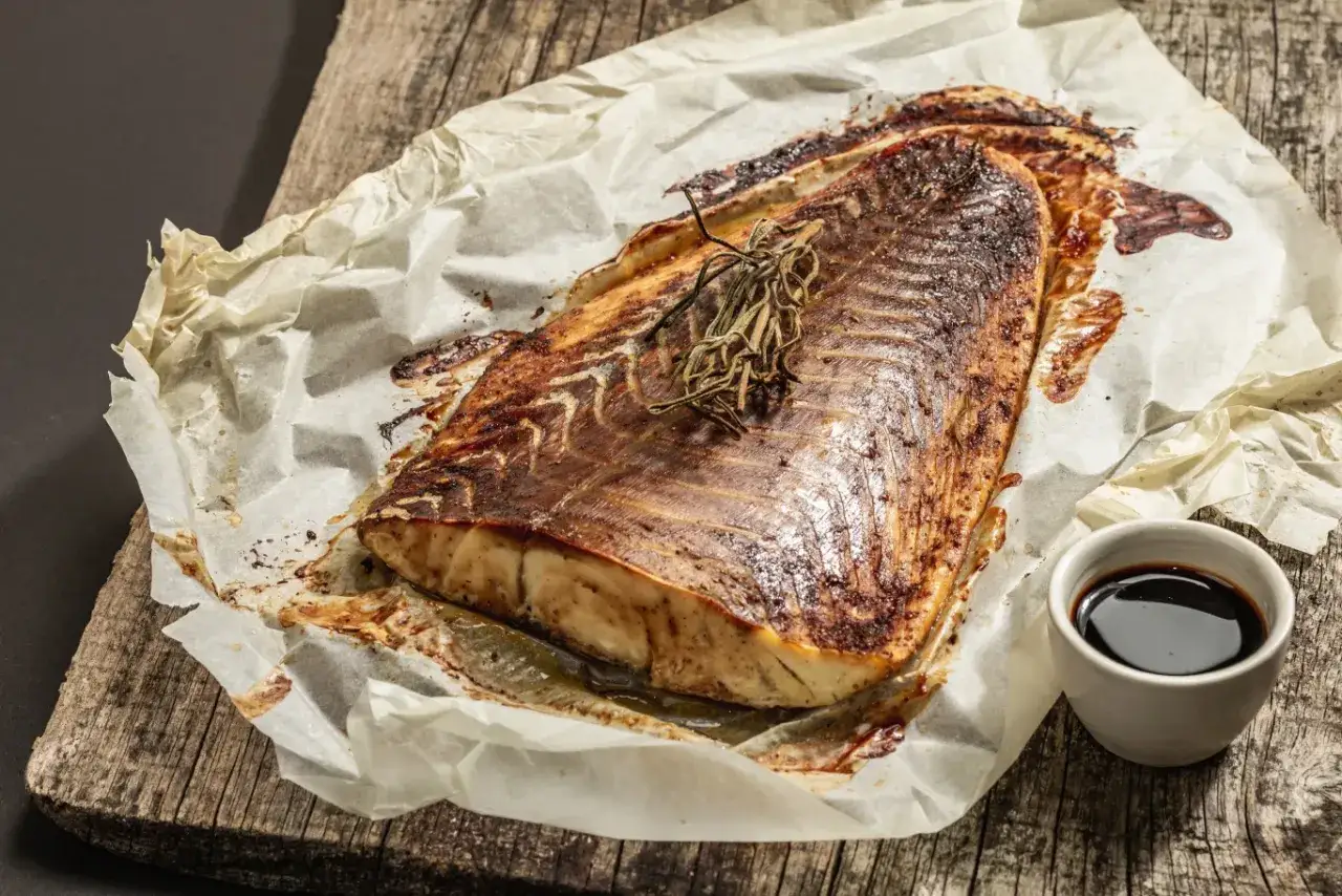 Pieczona ryba czerniak, aromatyczna i soczysta, podana na papierze do pieczenia z gałązką rozmarynu i sosem.