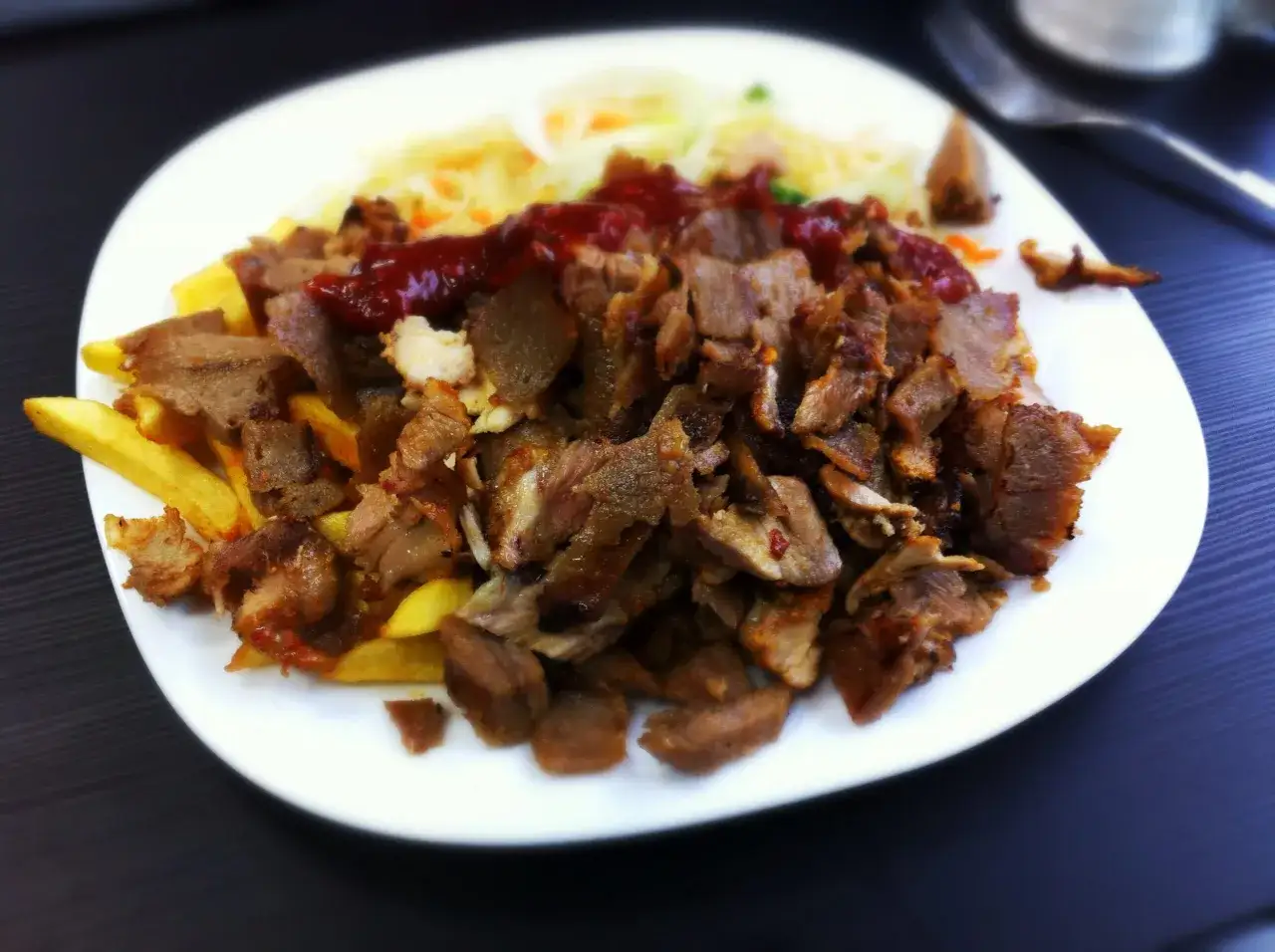 Talerz pełen soczystej baraniny w kebabie, podanej z chrupiącymi frytkami i surówką, polany sosem.