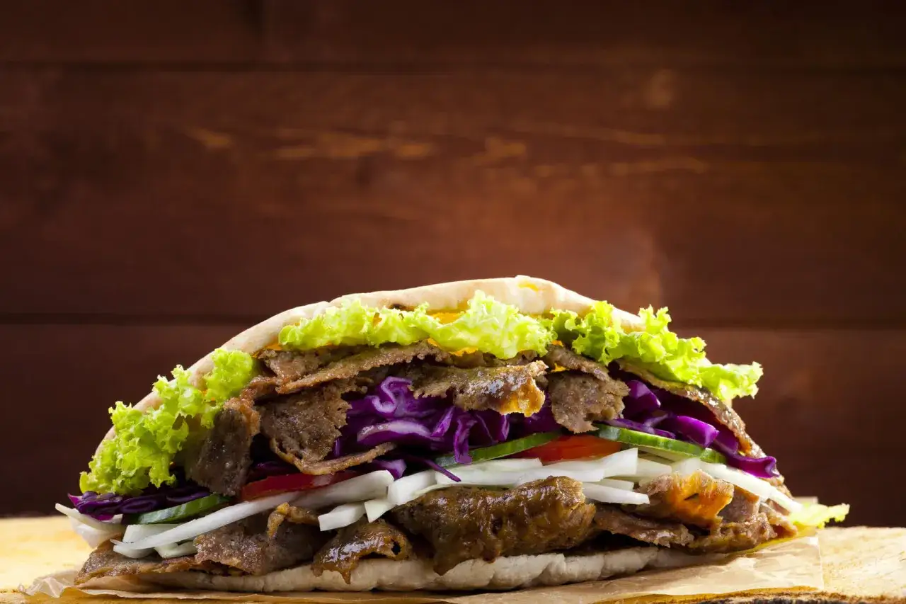 Pyszny kebab z soczystym mięsem, chrupiącą sałatą, czerwoną kapustą i świeżymi warzywami. Idealny skład na szybki posiłek.
