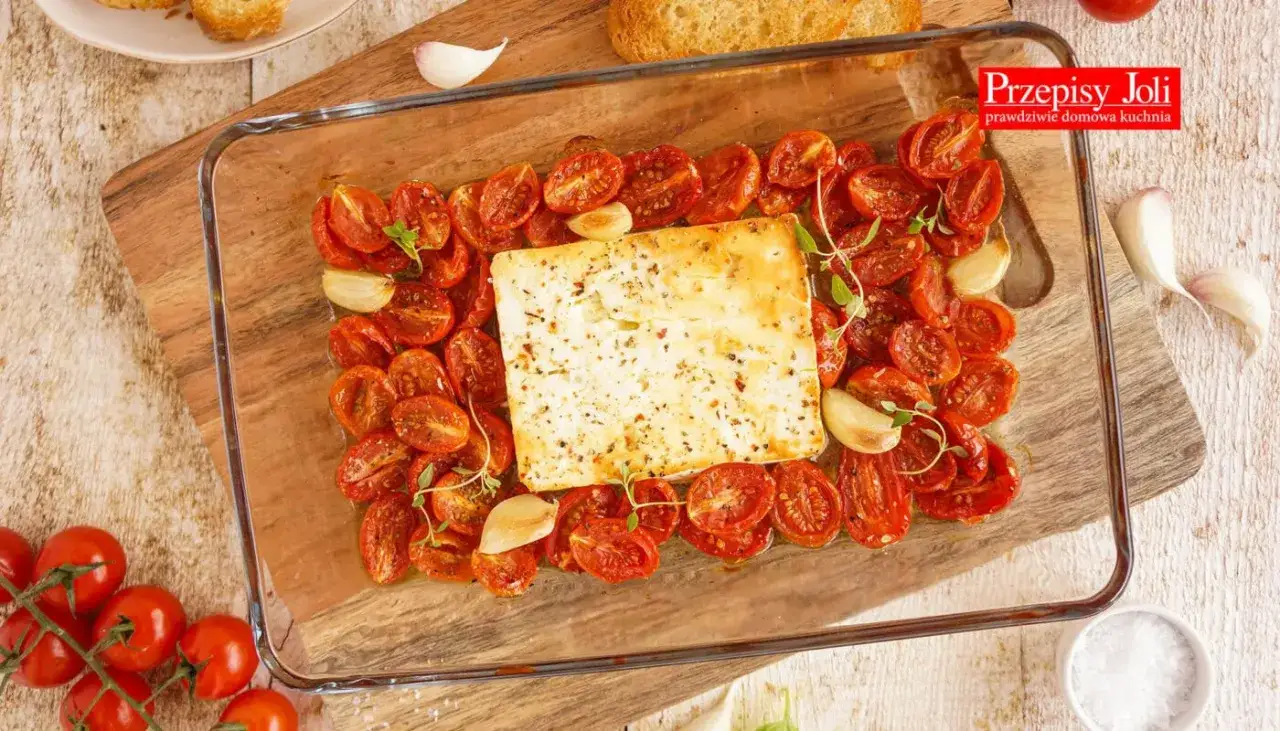 Pyszna pieczona feta otoczona pomidorkami koktajlowymi i czosnkiem, gotowa do podania z grzankami.