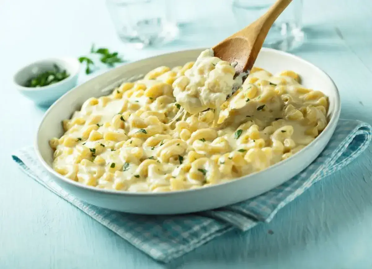 Kremowy makaron z serem, idealny przepis na mac and cheese. Drewniana łyżka nabiera porcję dania, ukazując ciągnący się ser.