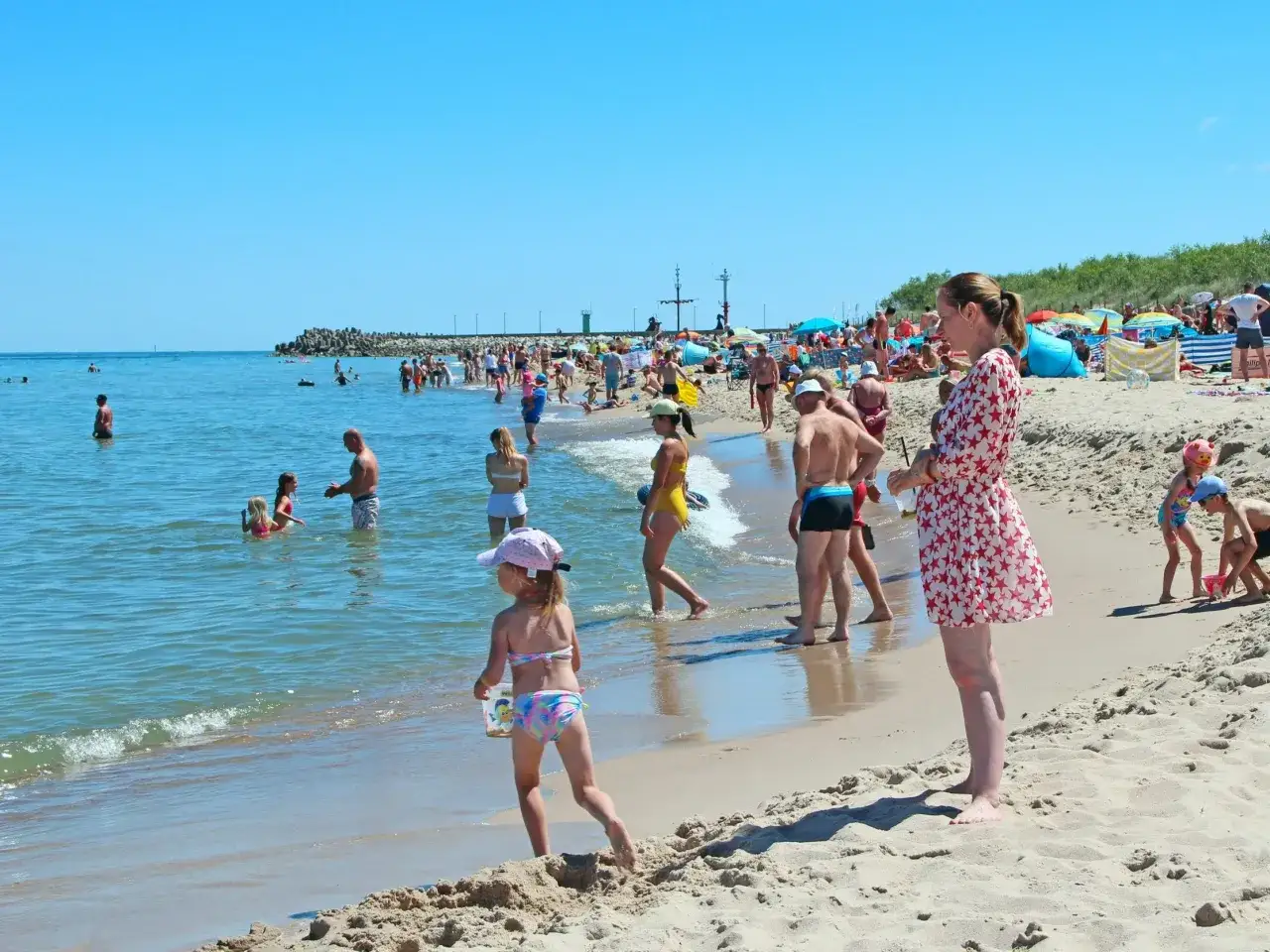 Słoneczny dzień nad Bałtykiem. Ludzie kąpią się w orzeźwiającej wodzie, inni odpoczywają na piaszczystej plaży.