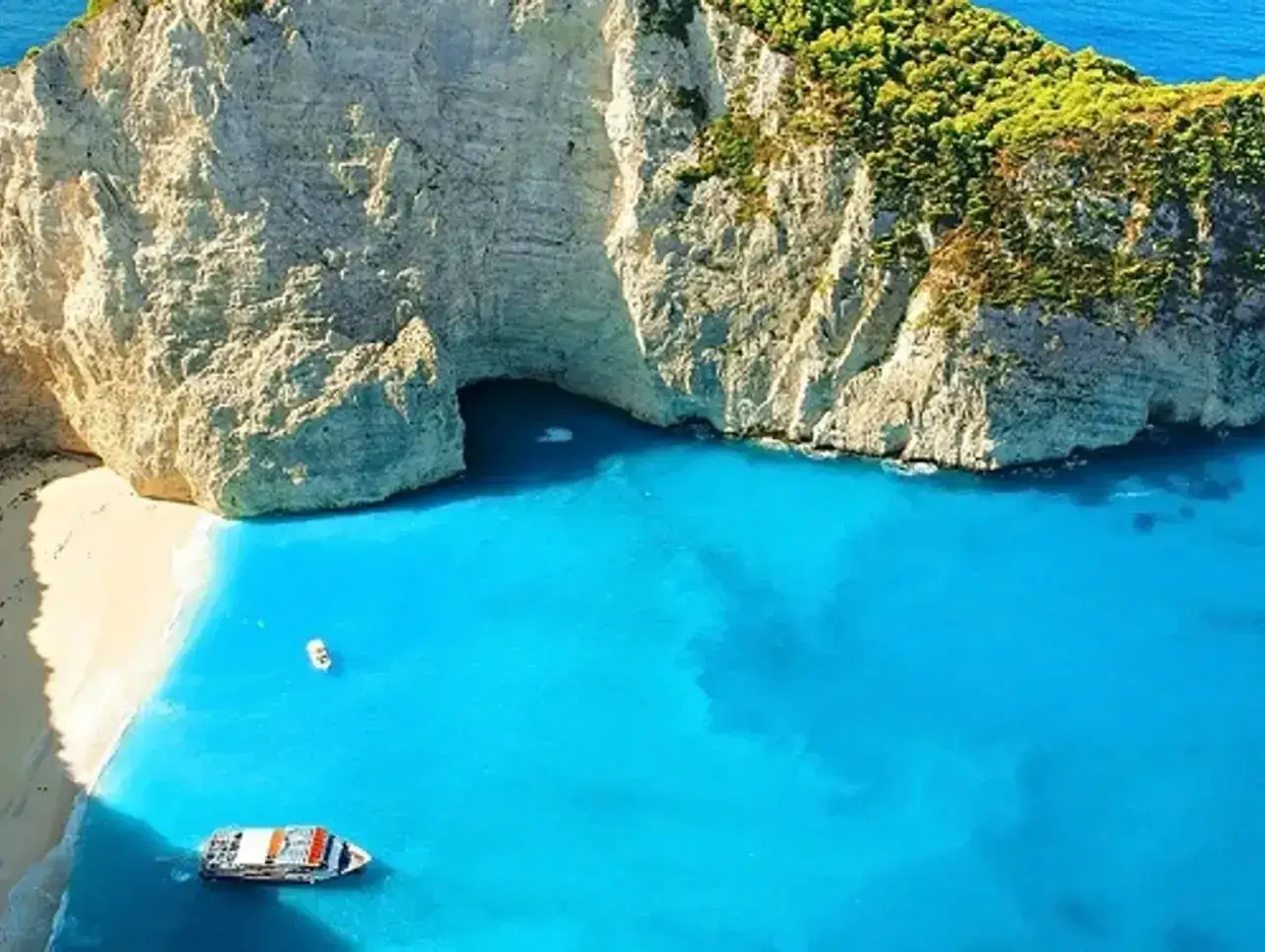 Zatoka Navagio na Zakynthos, jakie morze! Turkusowa woda otacza białą plażę i skalne klify. Dwa statki unoszą się na falach.