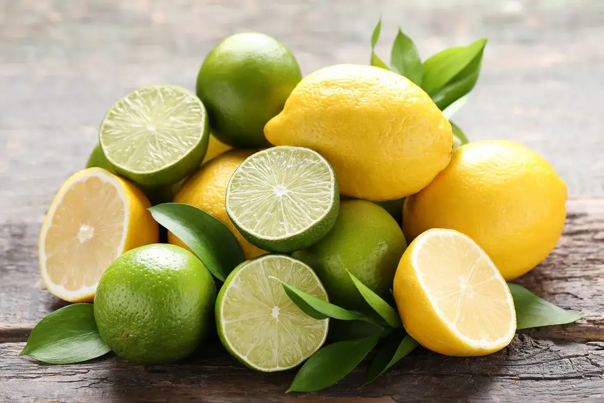 Stos świeżych, soczystych cytryn i limonek, niektóre przekrojone, z zielonymi listkami na drewnianym tle.