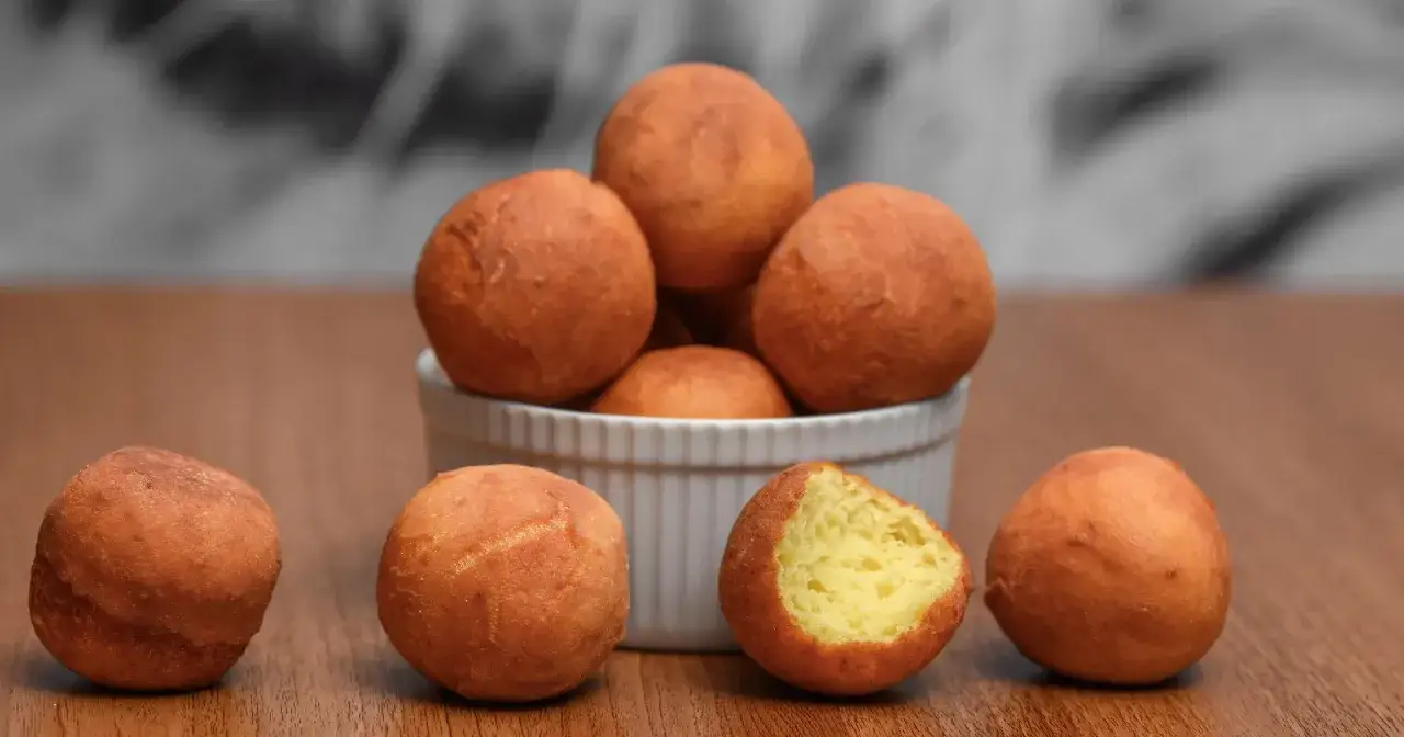 Złociste pączki w kształcie kulek, jeden nadgryziony, ukazujący puszyste wnętrze. Idealne na słodką chwilę, choć warto pamiętać o ich pączek kcal.